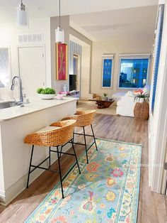 a kitchen and living room with an area rug in front of the counter, two bar stools on the floor