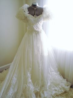 a wedding dress is displayed on a mannequin in front of a curtained window