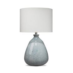 a gray table lamp with a white shade on the base and a light blue vase underneath it