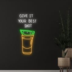 a neon sign that says give it your best shot on the wall next to a potted plant