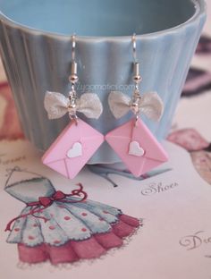 a pair of pink and white earrings with bows on them sitting next to a cup