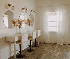 three mirrors on the wall in a room with white walls and wooden floors, along with four stools