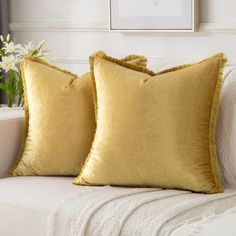 two yellow pillows sitting on top of a white couch next to a vase with flowers