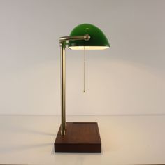 a green table lamp sitting on top of a wooden stand next to a white wall