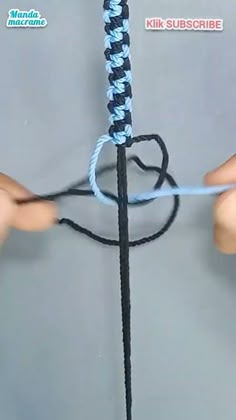 someone crocheting the end of a blue and black rope with two hands holding it