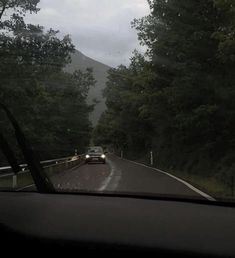 a car is driving down the road in front of some trees and mountains on a cloudy day