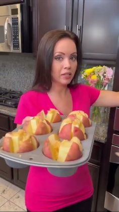 a woman holding a tray full of hot dogs and buns in the kitchen with flowers on the counter