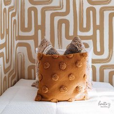 a brown pillow sitting on top of a bed next to a wallpapered wall