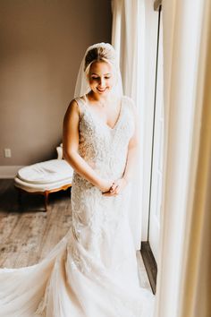 a woman in a wedding dress standing by a window