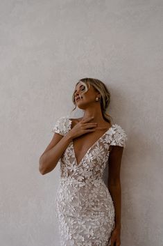 a woman in a white dress leaning against a wall with her hand on her chest