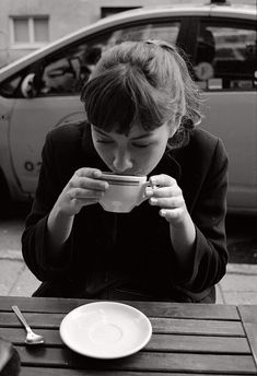 a woman sitting at a table drinking out of a cup with a spoon in front of her