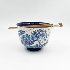 a blue and white bowl with chopsticks sticking out of the side on a white background