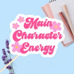 a sticker that says main character energy next to a notebook, pen and flowers