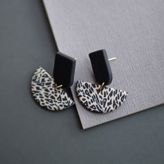 a pair of black and white animal print earrings on top of a gray surface with a grey background