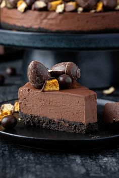 a piece of chocolate cheesecake on a black plate with nuts and candy around it