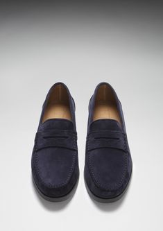 Here we offer you another Hugs & Co. take on a classic style. Our penny loafer upper made with carefully selected blue Italian suede is teamed with a robust boat shoe sole in slate grey rubber. This gives the shoes great wearability, fantastic comfort and the timeless style you're looking for in a penny loafer. We also offer loafers with tassels and driving shoes here at the Hugs & Co. online store. Our men's shoes are super cool and made to the tip top highest standards with leathers and suedes from England and Italy. If you're after preppy shoes or men's moccasins then you've come to the right place. UK Sizing Made in Portugal 100% Suede Upper featuring a 100% Leather Lining Rubber studded sole Navy Suede Loafers With Rubber Sole, Navy Suede Slip-on Loafers, Navy Slip-on Loafers With Leather Sole, Classic Blue Moccasins With Suede Lining, Classic Blue Moccasins With Brogue Detailing, Navy Suede Loafers For Formal Occasions, Classic Blue Loafers With Suede Lining, Blue Slip-ons With Suede Lining For Formal Occasions, Formal Slip-on Suede Boat Shoes