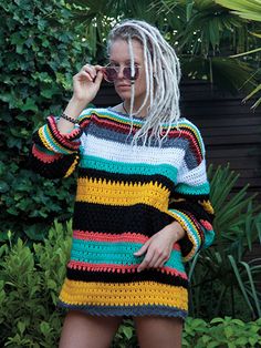 a woman with dreadlocks talking on a cell phone while wearing a multicolored crocheted sweater