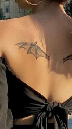 the back of a woman's shoulder with a bat tattoo on her upper arm