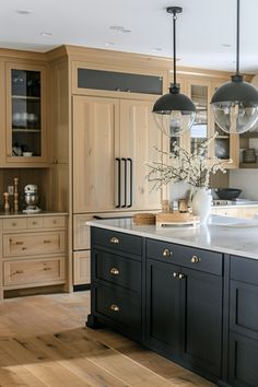 a kitchen with wooden floors and black cabinetry is pictured in this image, there are two pendant lights hanging over the island