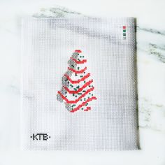 a cross - stitch christmas tree on a white cloth with red and green dots in the center