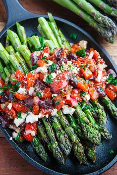 asparagus and tomato salad in a skillet on a wooden table with other vegetables