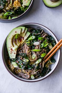 two bowls filled with noodles, greens and avocado