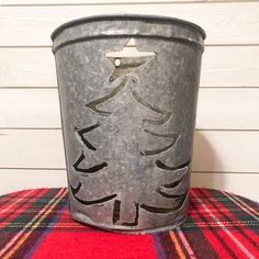 a metal bucket with a christmas tree painted on the side sitting on a plaid tablecloth