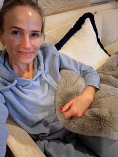 a woman sitting on a couch with a stuffed animal in her lap and smiling at the camera