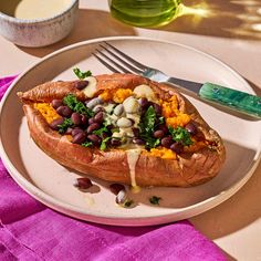 a white plate topped with a baked sweet potato covered in beans and veggies