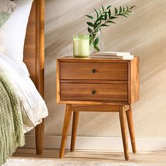 a nightstand with a candle on it next to a green plant and a white bed