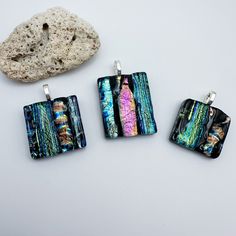 three square pendants sitting next to a rock