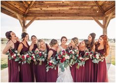 a group of women standing next to each other in front of a gazebo holding bouquets