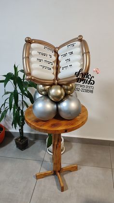 a table topped with silver and gold balls on top of a wooden stand next to a potted plant