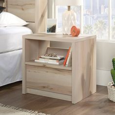 a nightstand with books on it next to a bed and cactus in a potted plant