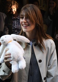 a woman holding a white stuffed animal in her hands and smiling at the camera while standing next to other people