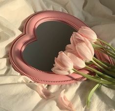 pink tulips in front of a heart shaped mirror on a white bed sheet