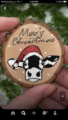 a hand holding a wooden ornament with a cow wearing a santa hat