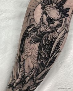 an owl tattoo on the arm with leaves and moon behind it, done by person in black and grey ink