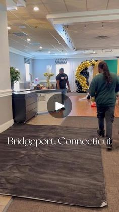 two people are walking in an office with carpet on the floor and one person is wearing a green shirt