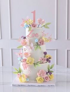 a three tiered cake decorated with flowers and the number one on it's side