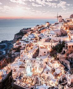 an aerial view of the white city of oia at dusk, with its lights on