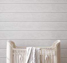 a white crib with a blanket on it in front of a wall that has wood planks