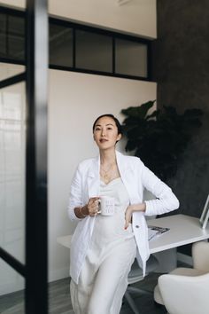 a woman standing in front of a desk holding a cup