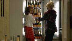 two women standing in front of an open refrigerator with beer bottles on the shelves behind them