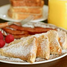 two plates with pastries, raspberries and bacon on them next to a glass of orange juice