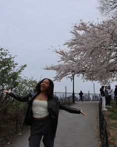 a woman in a black jacket and white top is walking down a path with her arms outstretched