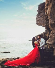 a man and woman standing next to each other near the ocean with rocks on either side