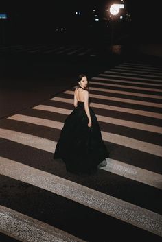 a woman in a long black dress crossing the street at night with her back turned to the camera