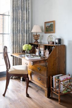 a wooden desk sitting in front of a window with a lamp on top of it