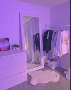 a bedroom with purple lighting and clothes hanging on the rack in front of a mirror